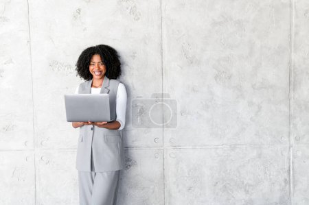 Mit einem Laptop in der Hand strahlt die afroamerikanische Geschäftsfrau eine ungezwungene, aber professionelle Atmosphäre aus und präsentiert eine Balance zwischen Komfort und Unternehmenserwartungen.
