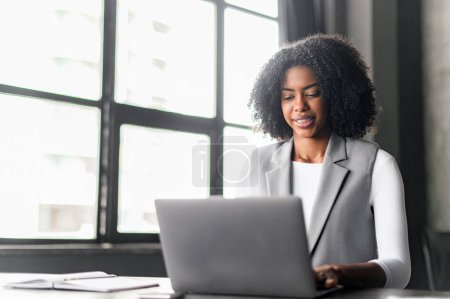 Eine fokussierte Geschäftsfrau arbeitet an einem Laptop, ein Bild der Konzentration und Hingabe, das das Engagement veranschaulicht, das in der heutigen schnelllebigen Geschäftsumgebung erforderlich ist..