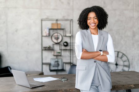 Photo for A beaming African-American woman stands confidently, her arms crossed, in a stylish business-casual vest and white long-sleeve shirt, representing a blend of modern professionalism and approachability - Royalty Free Image