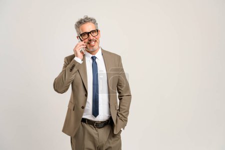 Confident senior businessman in professional attire actively participates in phone conversation, highlighting the importance of communication and experience in the business industry, standing isolated