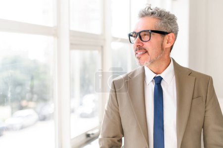An experienced mature grey-haired businessman looks thoughtfully into the distance in contemplation, a senior professional in a suit looking for inspiration or ideas. Concept of foresight and planning