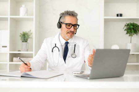 Oberarzt nimmt an einer Telemedizin-Sitzung teil, trägt ein Headset und einen weißen Mantel und spricht online während eines virtuellen Termins, einer Online-Beratung oder einer Patientennachsorge.