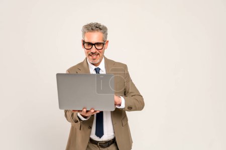 Un homme d'affaires charismatique aux cheveux gris qui regarde un écran d'ordinateur portable. Cette image capture l'essence des présentations commerciales modernes ou de la communication en ligne, parfaite pour les concepts liés à la technologie