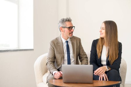 Un homme d'affaires chevelu a une discussion dynamique avec une jeune professionnelle dans un ordinateur portable dans un bureau minimaliste, illustrant l'échange mutuel d'idées et d'expertise.