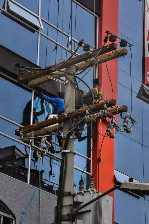 Téléchargez les photos : Des hommes connectent les lignes électriques de la ville : des ouvriers en électricité font des connexions dans un environnement urbain - en image libre de droit