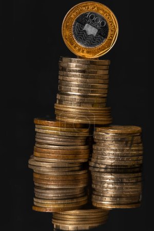 Goldmünzen und kolumbianisches Geld auf schwarzem Hintergrund: Investitions- und Finanzierungskonzept."