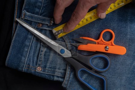Detail Jeans mit Schere und Maßband: Nähwerkzeuge auf Jeansstoff