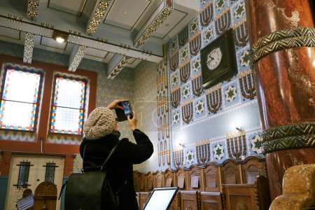 A woman captures a moment with her smartphone at the Kazinczy Street Synagogue in Budapest, blending modern technology with historic significance.