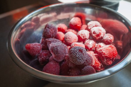 Großaufnahme von gefrorenen Erdbeeren in einer Aluminiumschüssel auf dem Küchentisch.