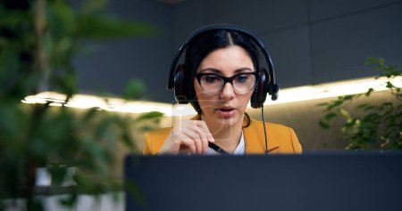 Photo for Likable confident successful smart adult woman in stylish clothes in headphones sitting in front of laptop during online webinar from specially decorated home office - Royalty Free Image