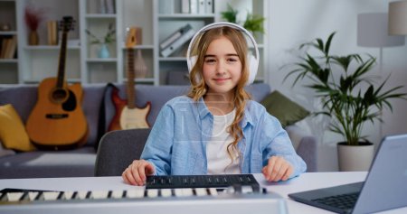 Photo for Portrait of preteen child girl learning to play music instrument and looking at camera. Beautiful little kid girl playing piano with headphones in living room or music school - Royalty Free Image