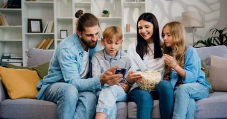 Photo for Parents father mother and cute little kids children watch funny social media video on mobile phone. Young family using modern wireless tech watching vlog, enjoy free time on internet. - Royalty Free Image