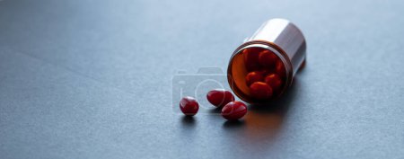 Téléchargez les photos : Red capsule pills and brown plastic bottle on dark background. Pharmacy banner. Prescription drugs. Health care and medicine. Pharmaceutical industry. Vitamin and supplement concept. Dose recommended. - en image libre de droit