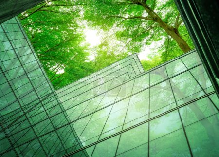 Foto de Edificio ecológico en la ciudad moderna. Edificio de oficinas de vidrio sostenible con árbol para reducir el calor y el dióxido de carbono. Edificio de oficinas con ambiente verde. Edificio corporativo reducir CO2. - Imagen libre de derechos