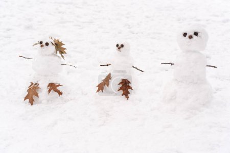 Foto de Lindos tres muñecos de nieve blancos de pie en el fondo cubierto de nieve durante el invierno. Concepto de temporada y vacaciones - Imagen libre de derechos