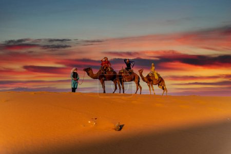 Photo for Three passengers and their handler travel in the Saharan Desert in Morocco - Royalty Free Image