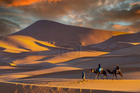 Two passengers and their handler travel in the Saharan Desert in Morocco