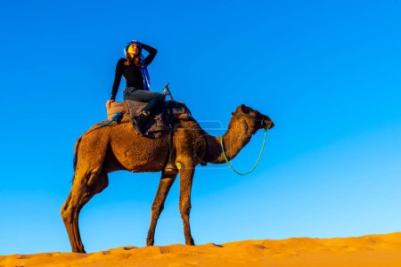 Téléchargez les photos : A beautiful model rides a camel through the Saharan Desert in Morocco - en image libre de droit
