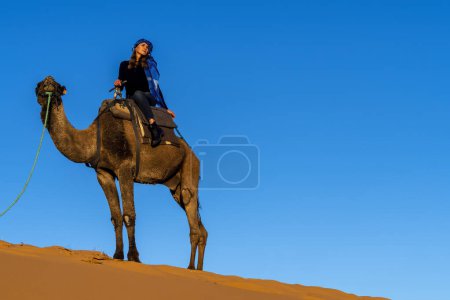 Photo for A beautiful model rides a camel through the Saharan Desert in Morocco - Royalty Free Image