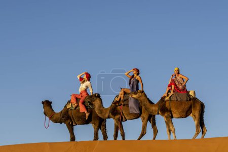 Photo for Three passengers and their handler travel in the Saharan Desert in Morocco - Royalty Free Image