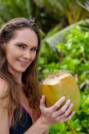 Sun-kissed brunette, adorned in a bikini, revels in Caribbean bliss on the sandy shores, combining beauty with adventure while hunting for coconuts