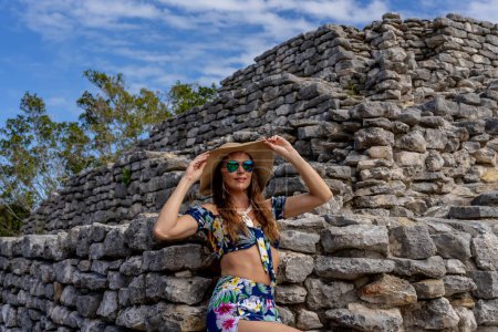 A radiant young woman explores the Xcambo Mayan ruins, her presence weaving elegance with ancient history, under the Caribbean sun's golden embrace