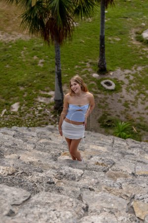 A radiant young woman explores the Xcambo Mayan ruins, her presence weaving elegance with ancient history, under the Caribbean sun's golden embrace