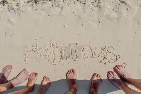 Photo for Friends' Caribbean Escape: Vacationers write 'Bahamas' in the sand, toes immersed, capturing sun-soaked moments on their idyllic beach retreat - Royalty Free Image