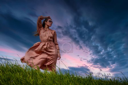 A gorgeous brunette model poses in a meadow on a windy spring day