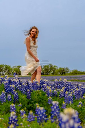 A beautiful brunette model enjoys a field of Bluebonnet flowers on a spring day