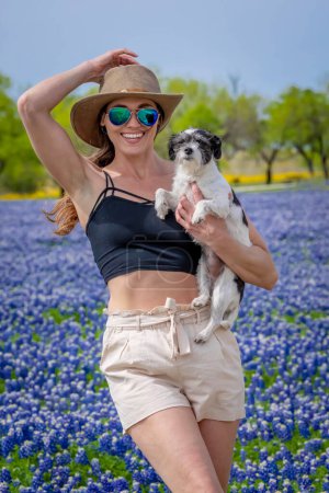 A beautiful brunette model enjoys a field of Bluebonnet flowers with her dog on a spring day