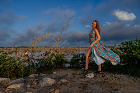 In the vibrant Mexican tropics, a stunning woman strikes a pose amidst lush greenery as the Yucatan sun sets, casting its golden glow on nature's canvas.