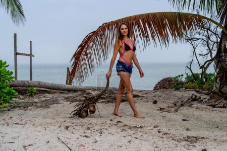 Sonnengeküsste Brünette, im Bikini, schwelgt in karibischer Glückseligkeit an den Sandstränden und kombiniert Schönheit mit Abenteuer bei der Jagd nach Kokosnüssen