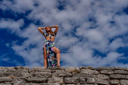 Eine strahlende junge Frau erkundet die Maya-Ruinen von Xcambo, ihre Anwesenheit webt Eleganz mit uralter Geschichte unter der goldenen Umarmung der karibischen Sonne