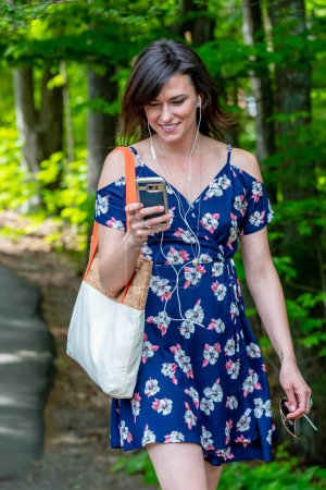 Eine brünette Studentin, in ihr Handy vertieft, geht flott zum Unterricht und navigiert nahtlos durch das Campus-Leben