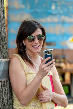 Une étudiante brune, absorbée par son téléphone portable, se dirige rapidement vers la classe, naviguant harmonieusement dans la vie du campus