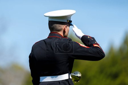 Photo for A poignant moment unfolds as a Marine plays taps, honoring a fallen veteran with a solemn salute, marking their internment at a national military cemetery. - Royalty Free Image