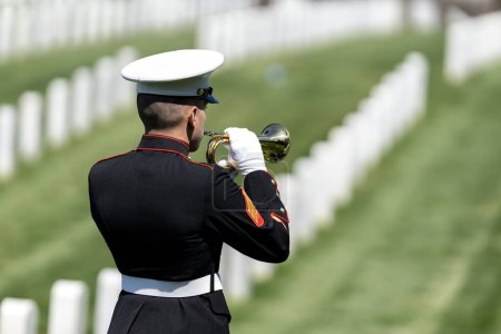 Photo for A poignant moment unfolds as a Marine plays taps, honoring a fallen veteran with a solemn salute, marking their internment at a national military cemetery. - Royalty Free Image