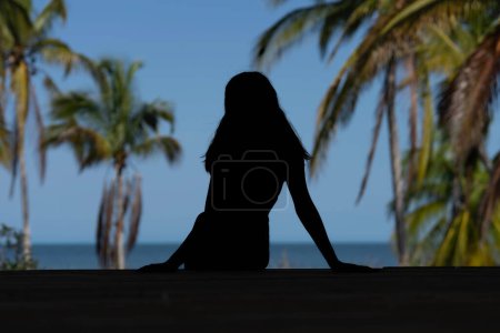 In the enchanting Caribbean, a radiant woman strikes a pose on a stunning beach, her silhouette graced by the vivid blue sky, embodying timeless beauty and coastal allure.