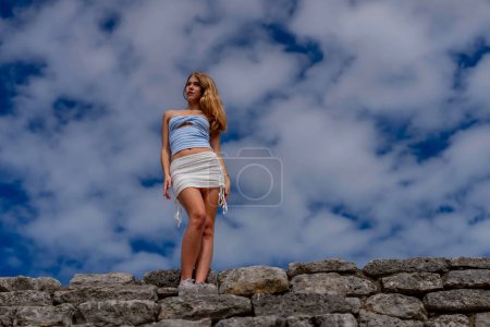 Eine strahlende junge Frau erkundet die Maya-Ruinen von Xcambo, ihre Anwesenheit webt Eleganz mit uralter Geschichte unter der goldenen Umarmung der karibischen Sonne