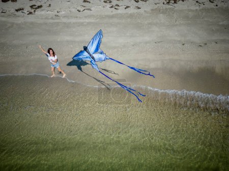 Une belle mannequin brune mature profite d'une journée à la plage tout en volant son cerf-volant près du rivage