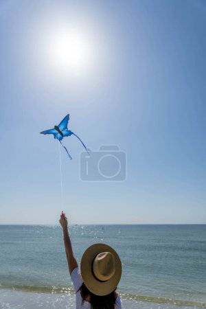 A beautiful mature brunette model enjoys a day at the beach while flying her kite near the shore