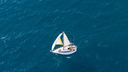 A small sailboat glides on clear Mediterranean waters near Malaga, Spain, under a serene summer sky.