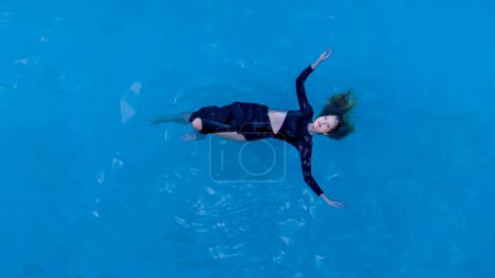 Capturada en una vista de pájaro, una mujer impresionante se desliza a través de una piscina cristalina junto a una orilla del Caribe, encarnando elegancia y felicidad en su escapada exótica