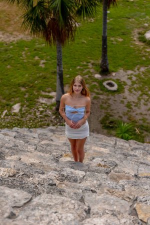 Una joven radiante explora las ruinas mayas Xcambo, su presencia tejiendo elegancia con la historia antigua, bajo el abrazo dorado del sol del Caribe
