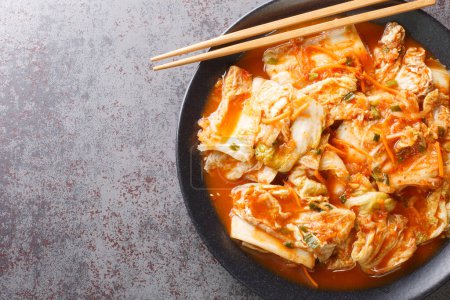 Téléchargez les photos : Kimchi, cornichon coréen de légumes épicés en gros plan dans un plat noir sur une table. Vue de dessus horizontale d'en haut - en image libre de droit