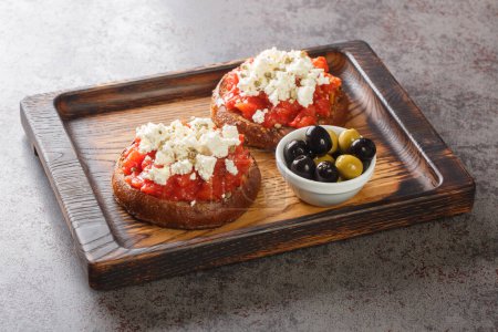 Foto de Aperitivo griego dakos con cebada rusk, tomates, queso feta, orégano y aceite de oliva primer plano en la tabla de madera sobre la mesa. Horizonta - Imagen libre de derechos