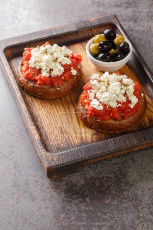Foto de Dakos Cretan Meze aperitivo con cebada rusk, tomates, queso feta, orégano y aceite de oliva primer plano en la tabla de madera sobre la mesa. Vertica - Imagen libre de derechos