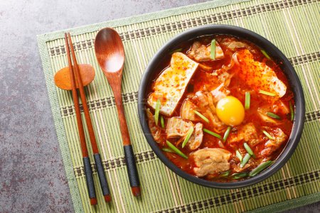 Photo for Sundubu Jjigae or soft tofu stew, is a traditional Korean dish made with silky soft uncurdled tofu coated in a spicy and flavorful broth closeup on the bowl. Horizontal top view from abov - Royalty Free Image