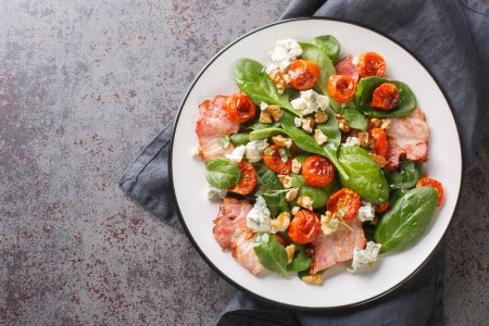 Photo for Warm french salad with bacon, spinach, roquefort cheese, walnuts, tomatoes, basil and garlic close-up in a plate on the table. Horizontal top view from abov - Royalty Free Image